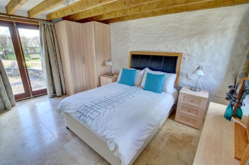 The delightful double bedroom has a beamed ceiling and patio doors to the garden