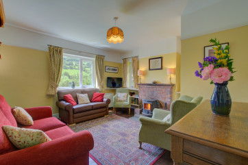 The cosy sitting room has an open fire and is furnished and decorated in traditional style