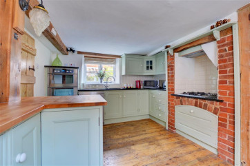 View into the kitchen showing the gas hob set into the area of the old fireplace, window above sink, double oven and a range of kitchen units.
