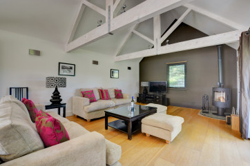 Open plan sitting room with comfortable seating, woodburner and doors to the garden