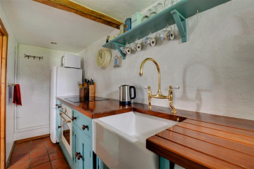 Small galley kitchen with cottage styed kitchen cupboards, wooden work surfaces and butler styled sink.
