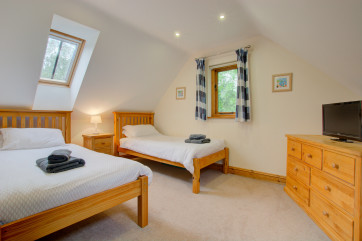 Twin-bedded room with sloping ceiling and comfy armchair.