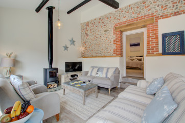 Open plan living room with comfortable seating, woodburner, tv & exposed brickwork
