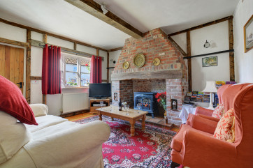 The sitting room is attractively furnished with comfortable seating, a lovely inglenook fireplace with an electric woodburner-style fire and beamed ceilings
