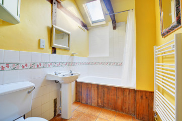 View showing white sanitary ware, daffodil yellow walls, and velux window above bath.
