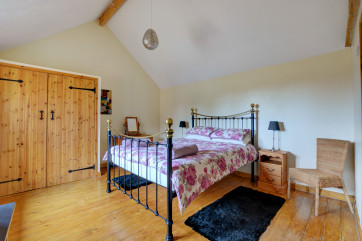 Double bedroom has plain linen with contrasting throw.  Plenty of storage in large pine wardrobe.  Wooden floors with rugs to the side of the bed for comfort.