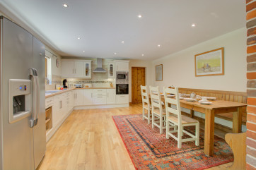 White fronted cupboards, stainless steel cooker and hob. Large dining table on rug on wooden floor.