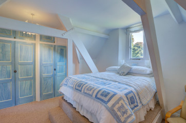 Bedroom One is furnished with a raised double bed, built in wardrobes and a chest of drawers.  There is a sloping ceiling and exposed beams.  A gothic window offers countryside views.