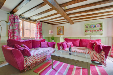 Lovely cottage living room, with a pretty colour scheme of natural, green and raspbery soft furnishings and comfortable seating.
