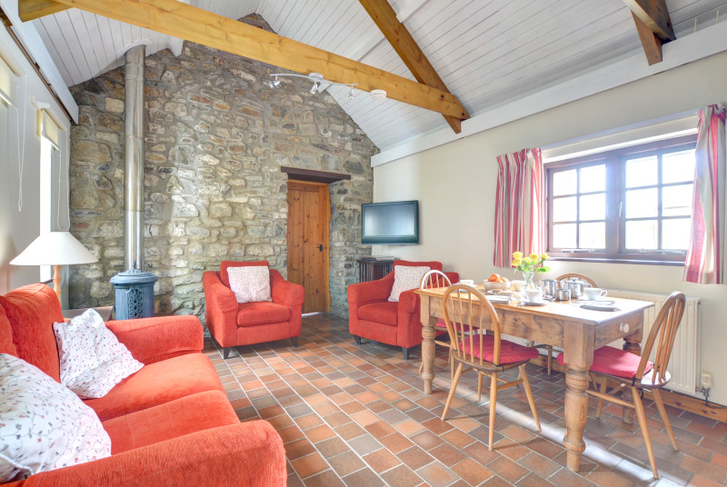 The living room has rugs over quarry tiled flooring, dining table and four chairs, comfortable three piece suite and a woodburning stove