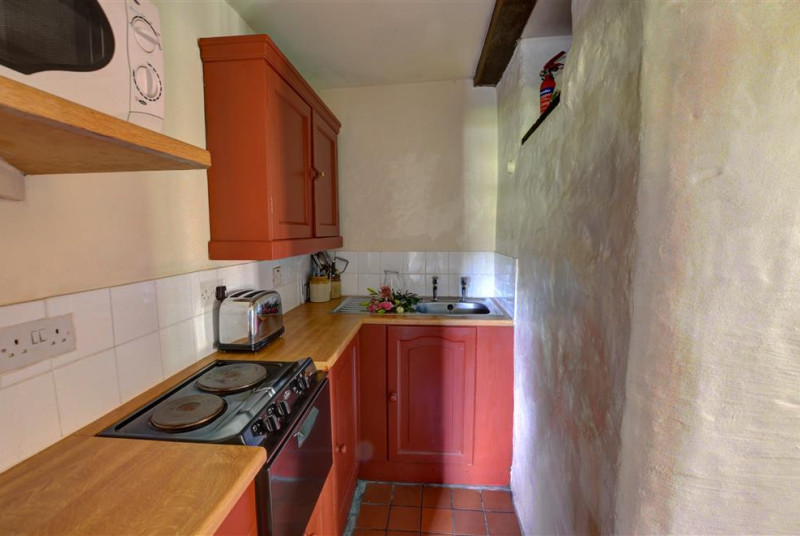 The kitchen is galley style, with a solid stone wall to one side, and quarry tile flooring
