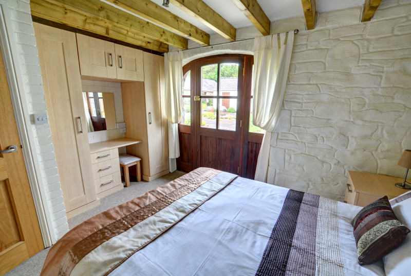 The double bedroom has a beamed ceiling and original stone wall, fitted wardrobes
