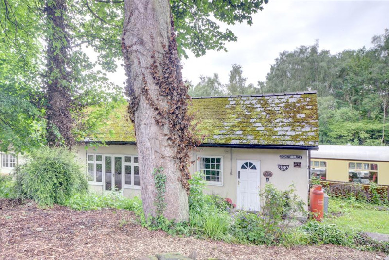 Cottage with steam train carriages behind it.