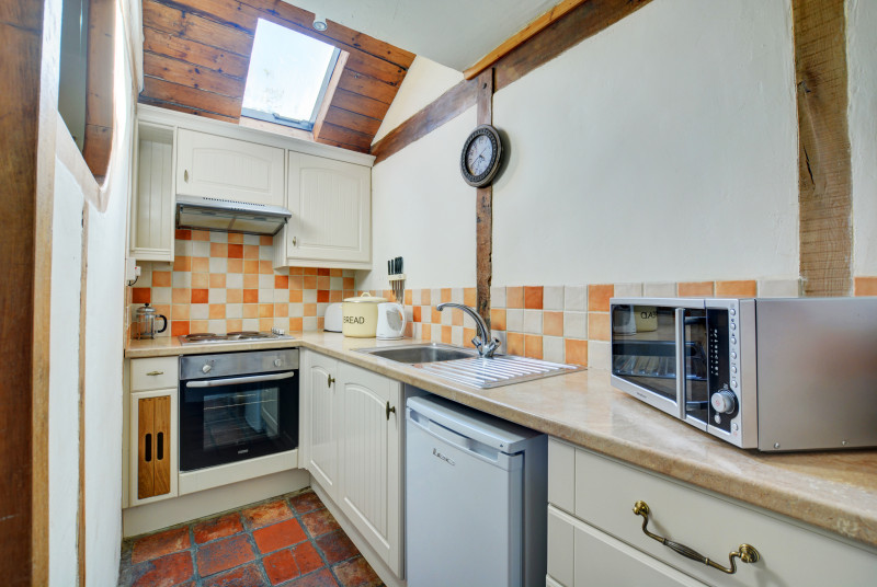 Compact and well presented kitchen with velux window, shades of cream beige and terracotta floor tiles.