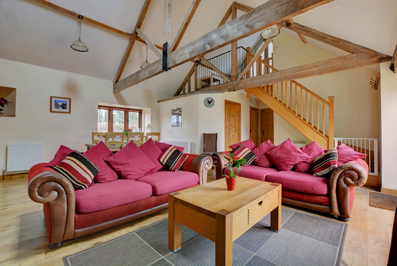 View of the comfortable sitting room with large colourful sofas and open beams.  Coffee table between sofas for drinks and books.  Open plan stairs to first floor.