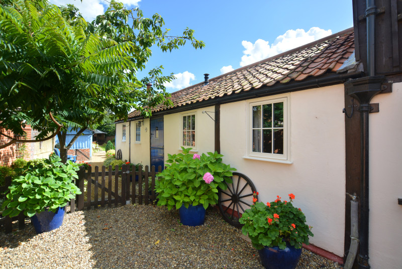 Pretty front view, with gravelled pathway, picket fencing and small tree.