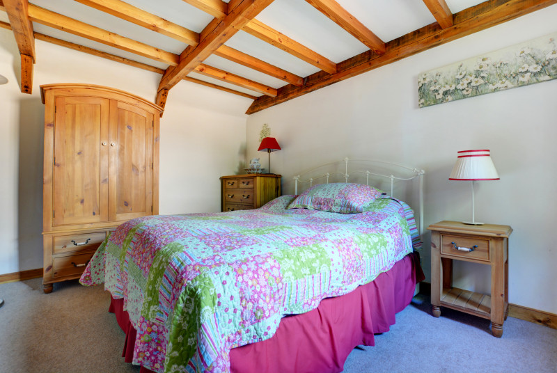 Very pretty country styled bedroom wtih beams, pine furniture, wrought iron bed and floral bedlinen in blues and pink.