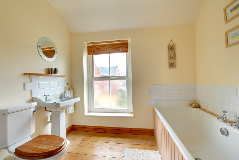 The bathroom is large and traditional with a window looking to the front of the property and wooden floor