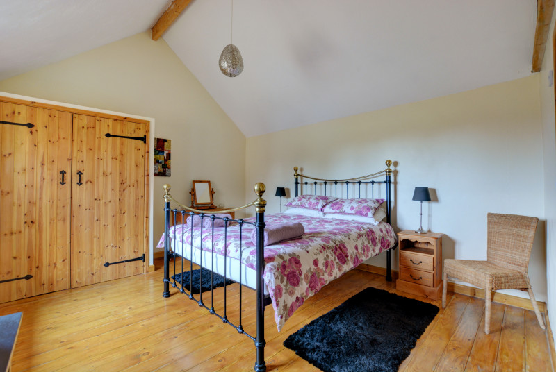 Double bedroom has plain linen with contrasting throw.  Plenty of storage in large pine wardrobe.  Wooden floors with rugs to the side of the bed for comfort.