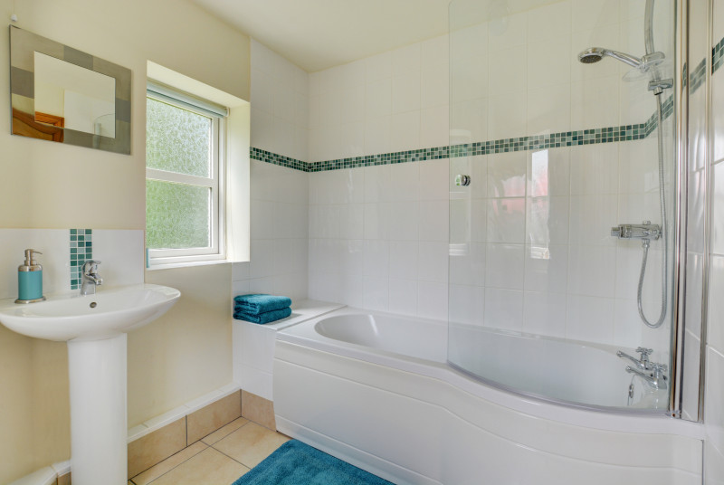 A contemporary white bathroom suite.  A bath with shower overhead.