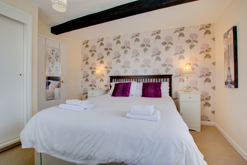 Double bed with bedside cabinets & lighting. Beam in ceiling shows character of property.
