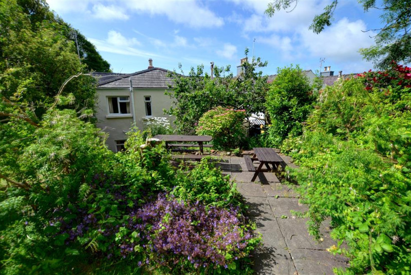 In the back garden is a small paved terrace with picnic tables and a sloping grass