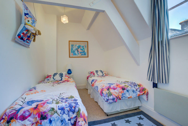 Bedroom Two is furnished with zip and link single beds and chest of drawers units.  There is a sloping ceiling and exposed beams. A window to the rear gives views over the inner cobbled courtyard.