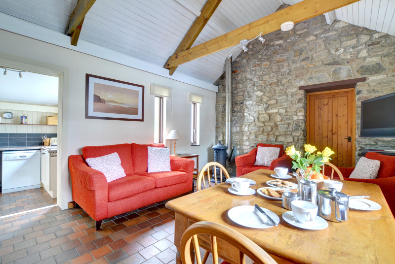 The living room has rugs over quarry tiled flooring, dining table and four chairs, comfortable three piece suite and a woodburning stove